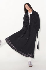 Waist-cinched, straight-cut, with a plaid patchwork design and raglan sleeves, this trench coat features a bold silhouette.